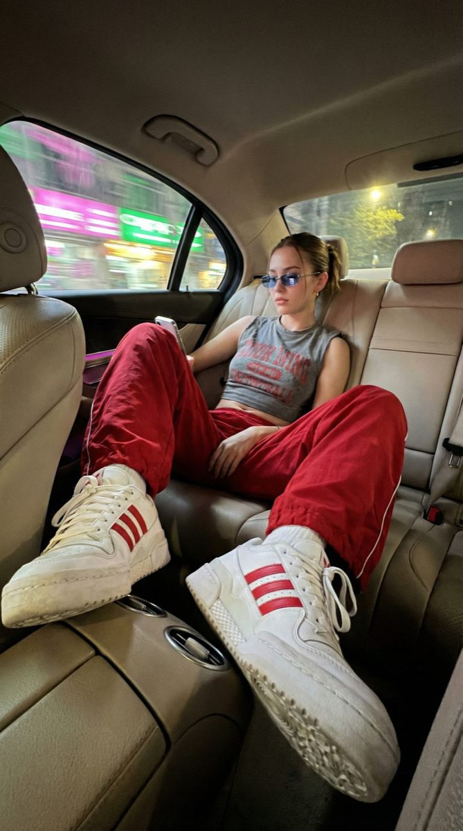 AI generated — iPhone night shot inside car backseat, woman in red track pants, sneakers foreground, city lights blur